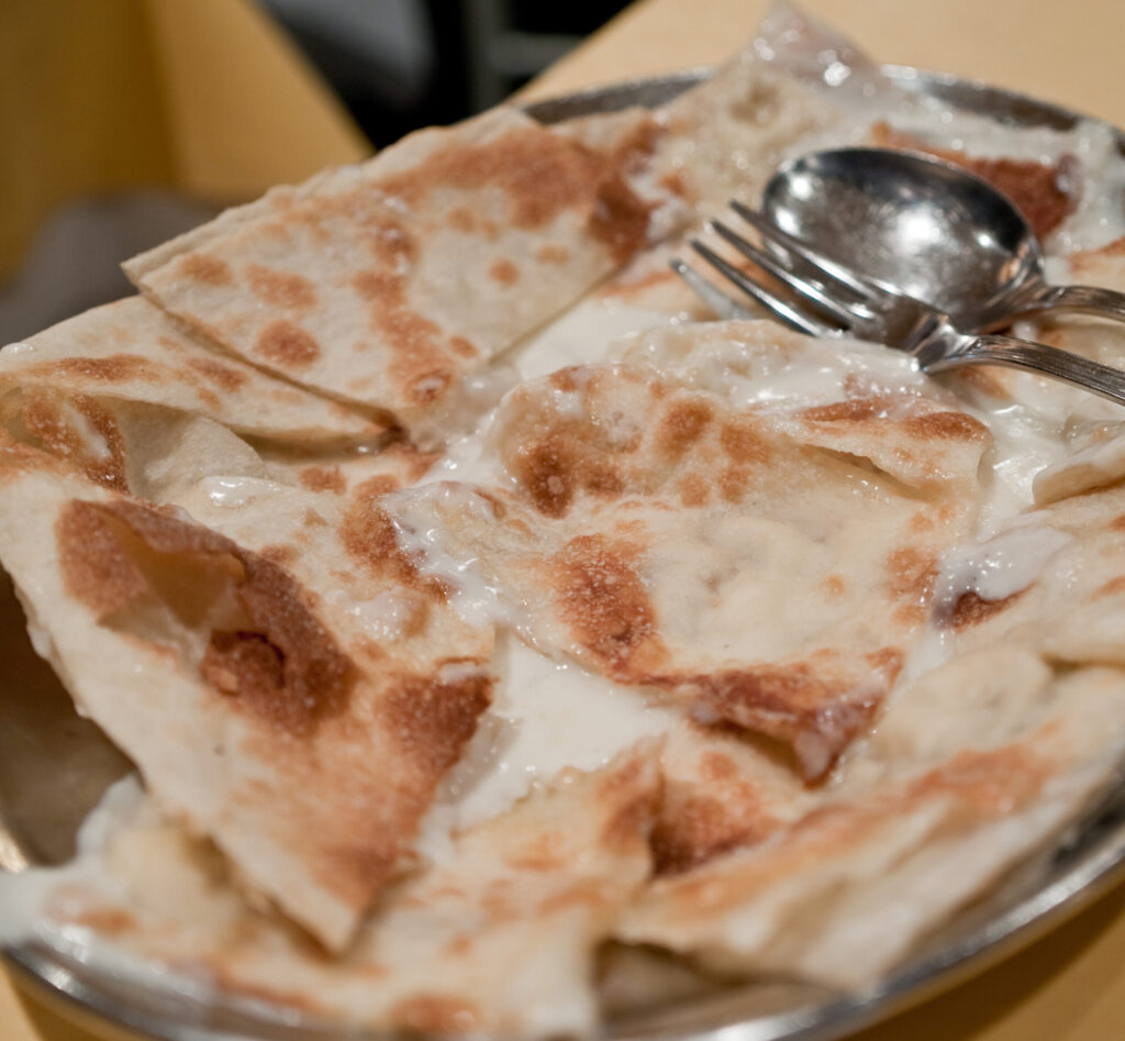 Traditional Focaccia di Recco with cheese, showing the translucent sheet and crescenza melted through the golden bubbles