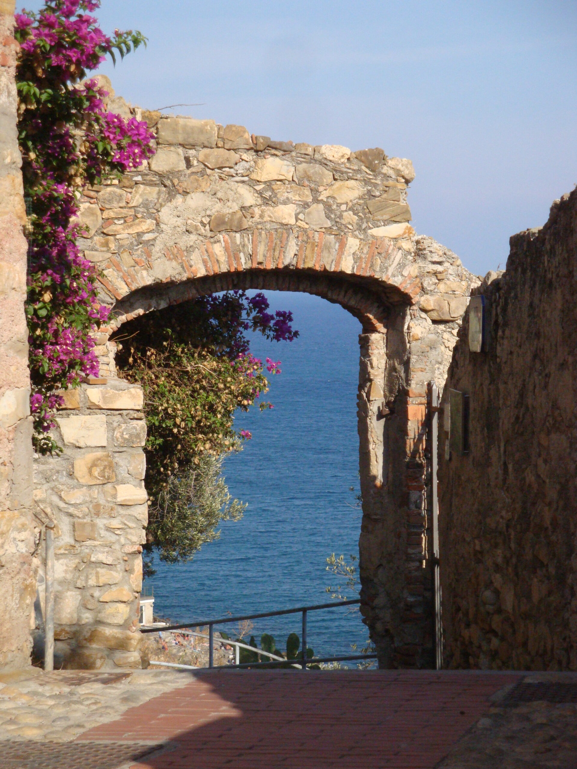 Un arco di pietra con bougainville nei carruggi di Cervo si apre sulla vista del mare