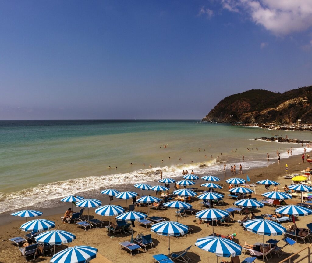 La spiaggia di Levanto con ombrelloni azzurri, il mare turchese e il promontorio del Mesco sullo sfondo