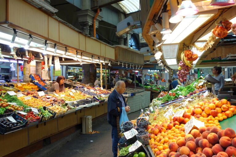 Interno del Mercato Orientale di Genova con banchi colorati di frutta e verdura sotto la copertura ottocentesca