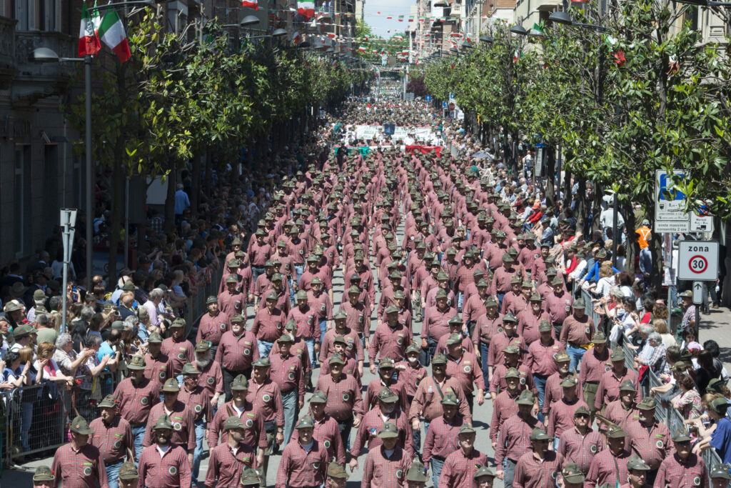 Aerial view of the National Alpini Rally parade, a sea of feathered hats marching down the main avenue