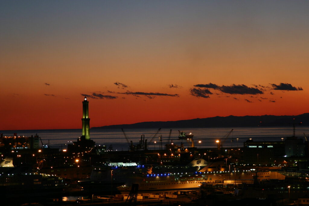 The illuminated Lanterna of Genoa stands out against the red sky of sunset over the harbour