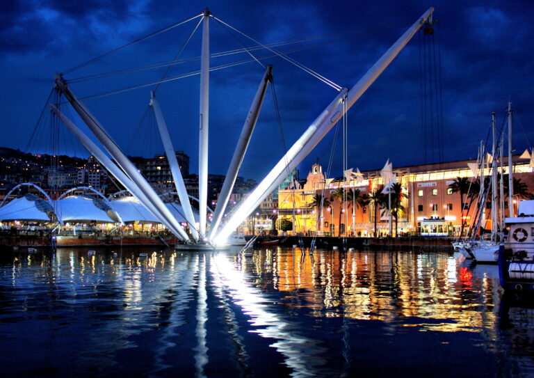 Il Porto Antico di Genova illuminato al crepuscolo, con il Bigo riflesso sull'acqua