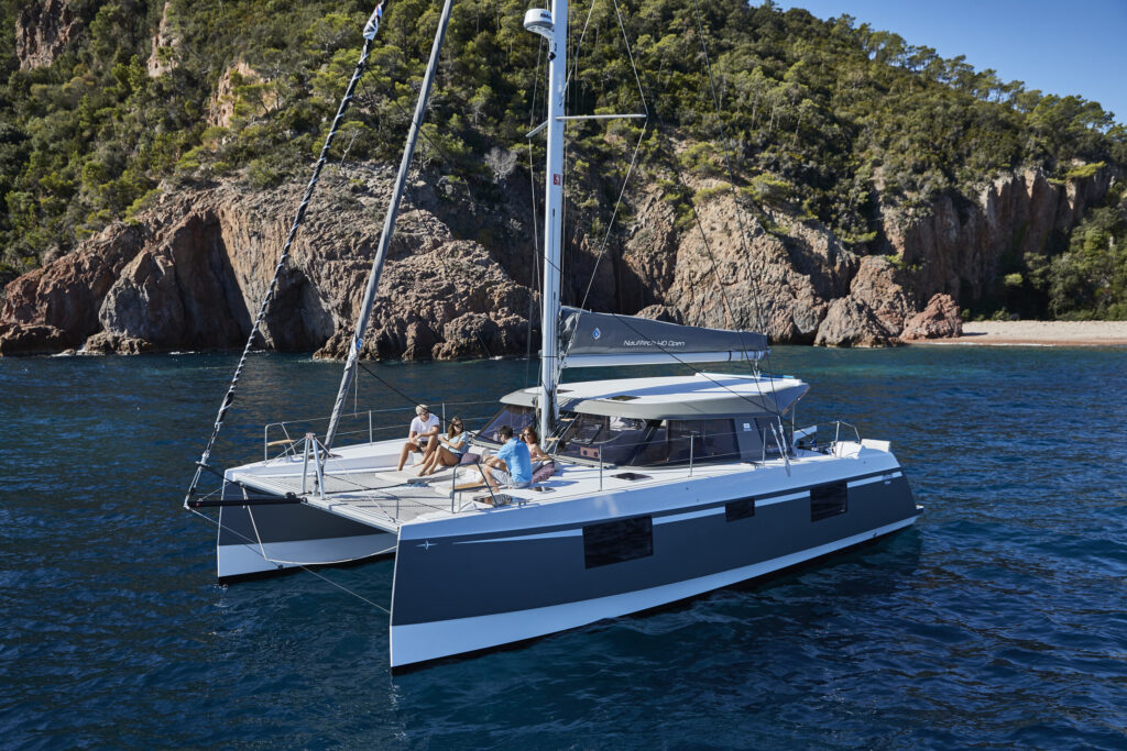 Un catamarano a vela all'ancora in una caletta rocciosa, con ospiti che si rilassano sul trampolino di prua