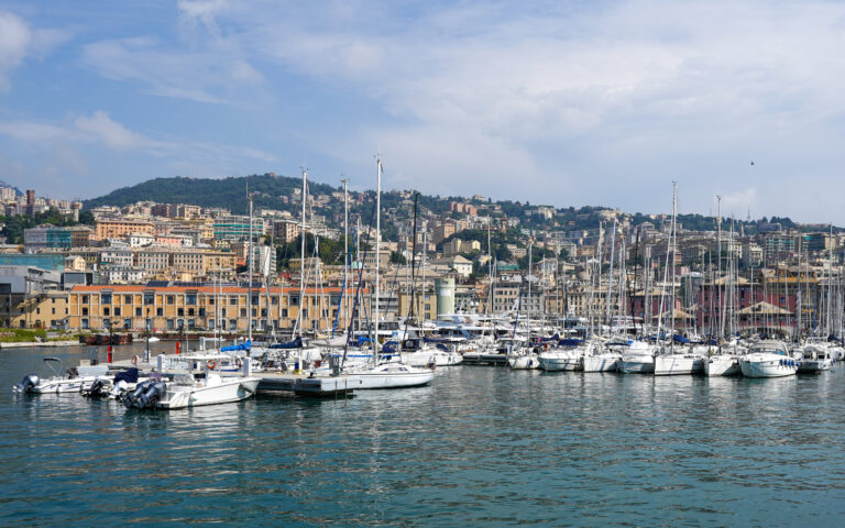Barche a vela nella marina del Porto Antico di Genova con la città sulle colline