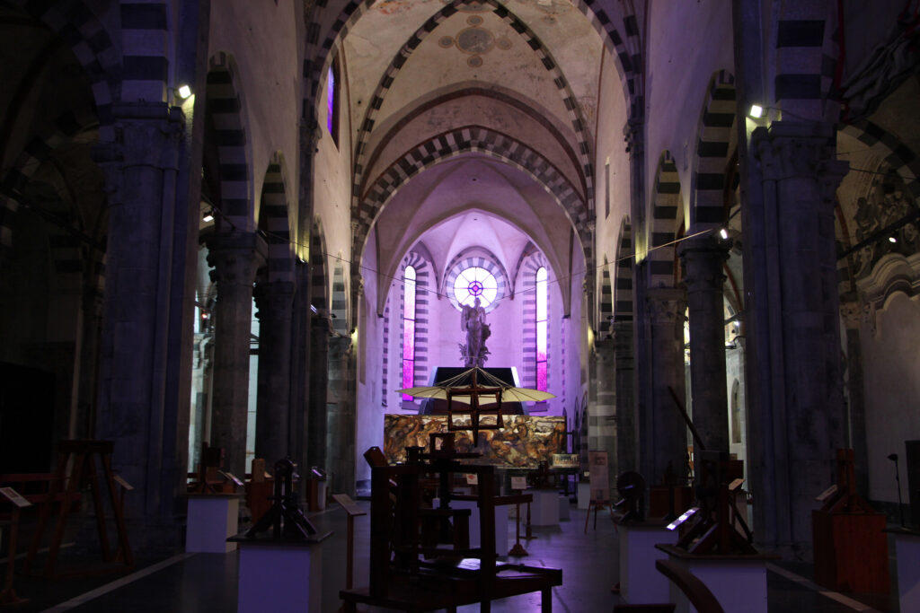 Navata della chiesa sconsacrata di Sant'Agostino a Genova, con gli archi a fasce bianche e nere e modelli di macchine in legno esposti per una mostra